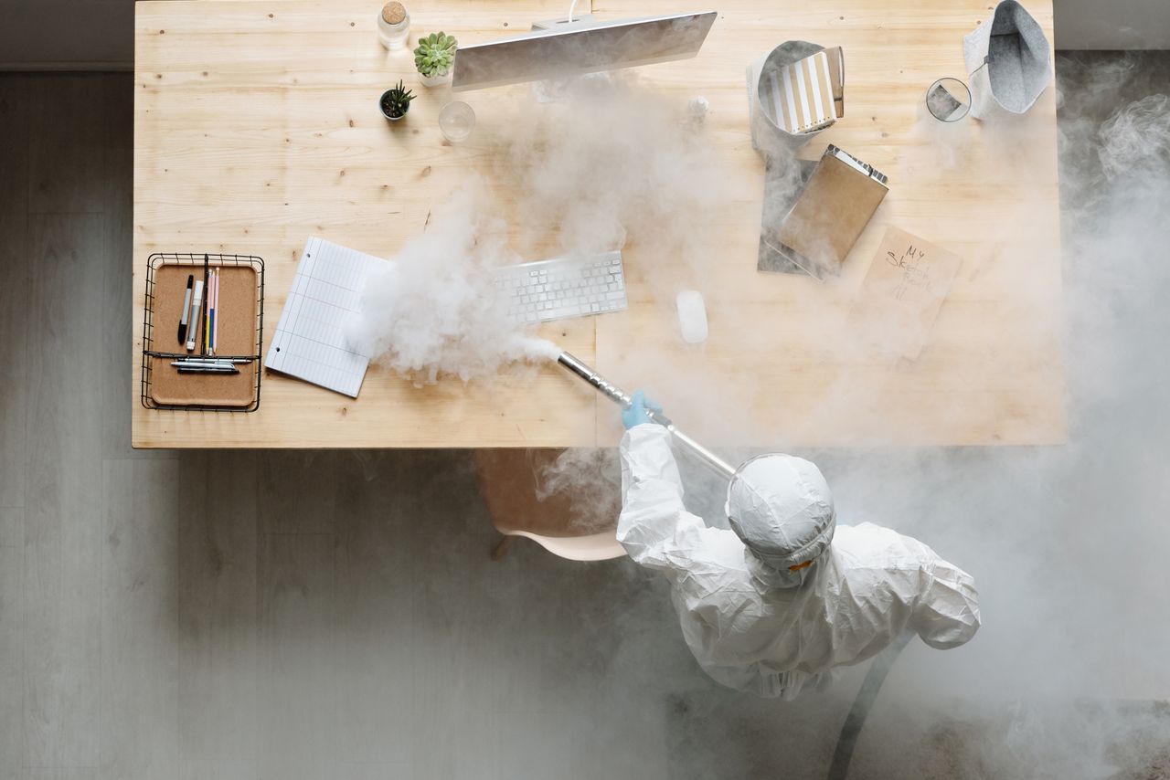 services-03 An individual disinfects a workspace using fumigation, wearing full protective gear for safety.