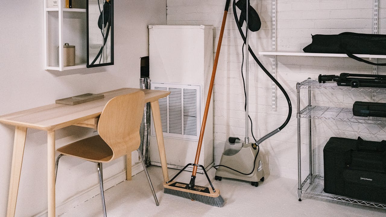hero-img-01 A tidy home office space featuring a wooden desk, chair, broom, and cleaning equipment.