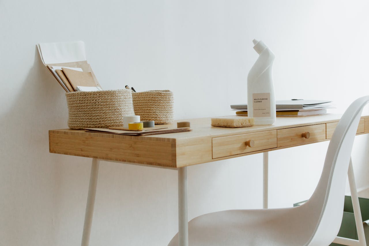 about-01 A clean and organized home office desk with cleaning products, papers, and storage baskets.